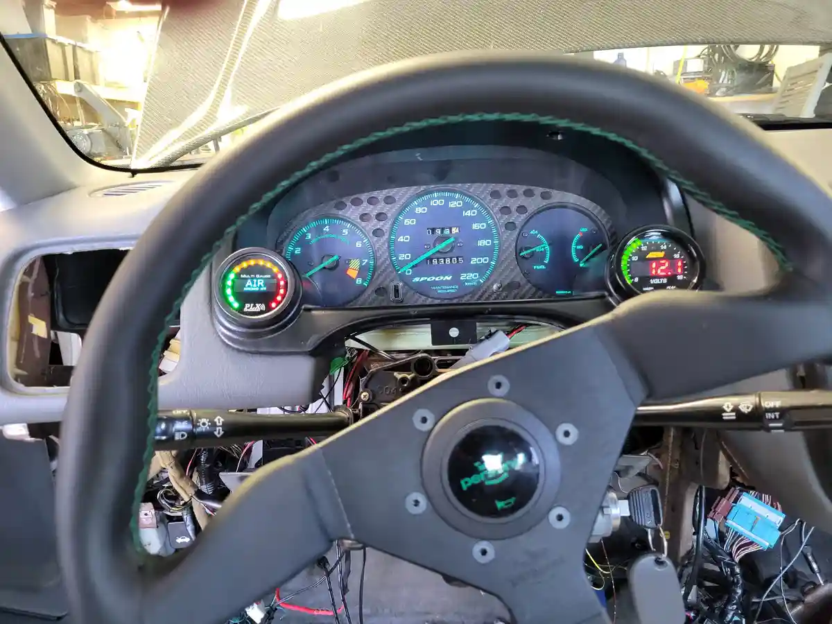 A car's dashboard and steering wheel are shown with the steering wheel partially removed, exposing wiring and components…