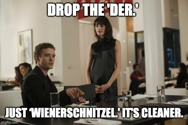 A man in a black suit sits at a restaurant table, gesturing toward a standing woman in a black dress. The overlaid text…