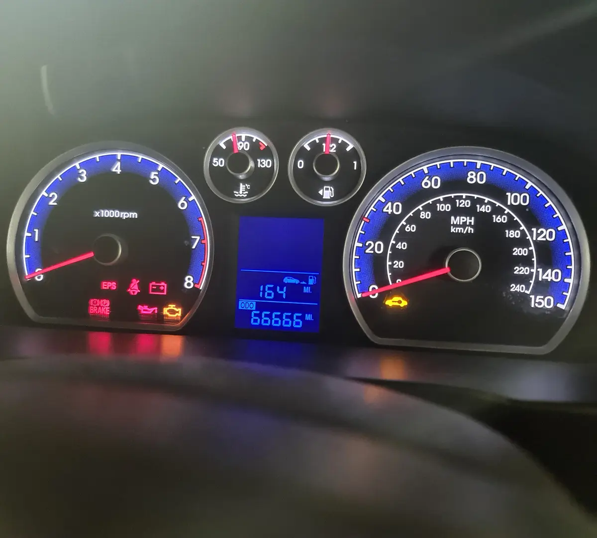 A car's dashboard shows a digital odometer reading '66666 MI' with multiple warning lights illuminated, including the check…