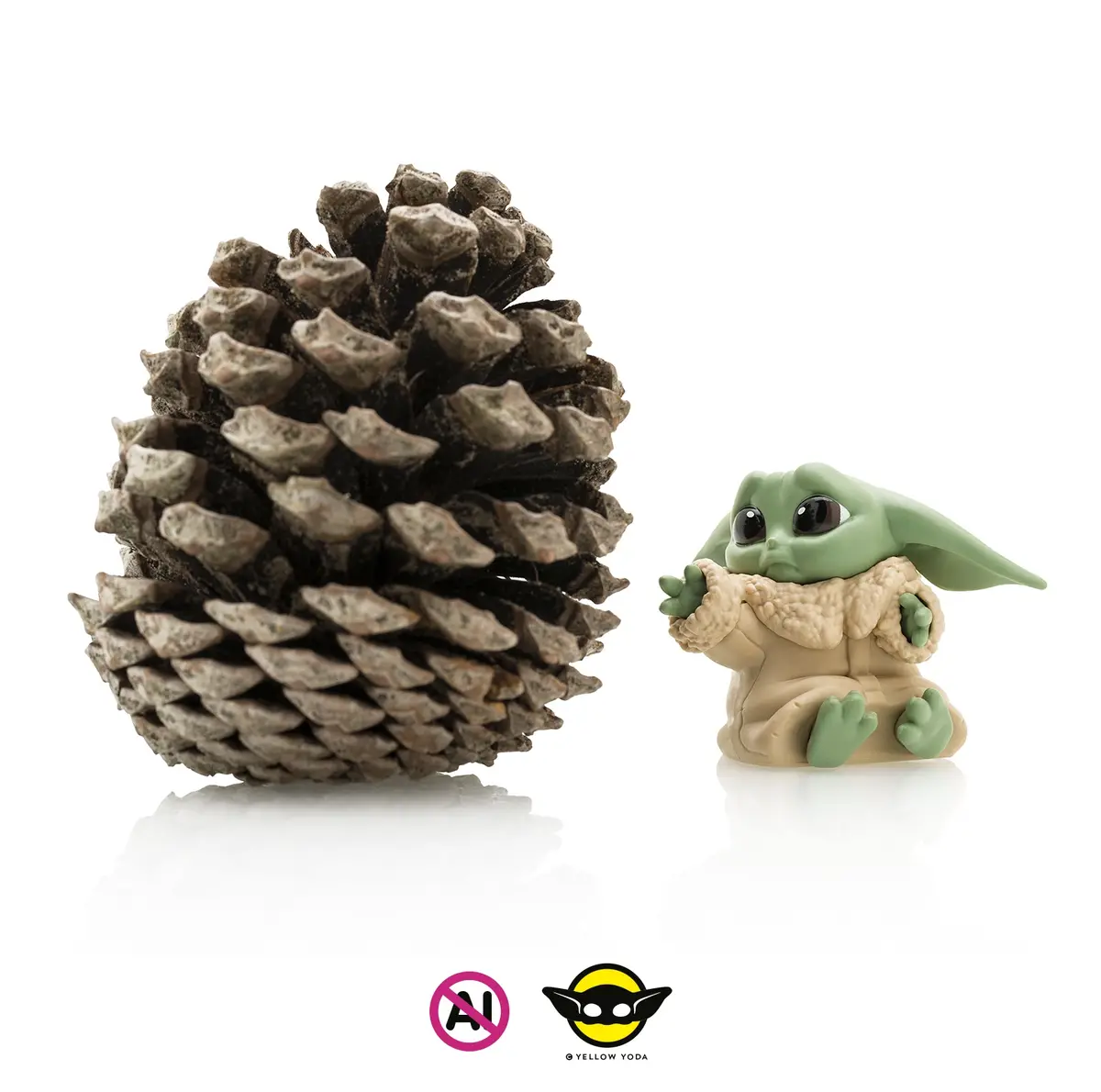 A small green baby yoda figurine sits beside a large pinecone on a white reflective surface. The baby yoda has large eyes…