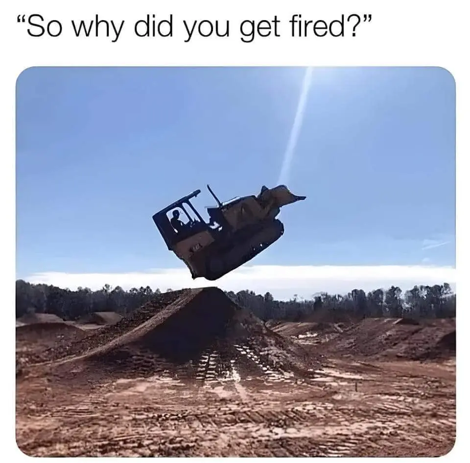 A bulldozer is captured mid-air, having launched itself off a dirt mound in a construction or quarry site under a clear blue…