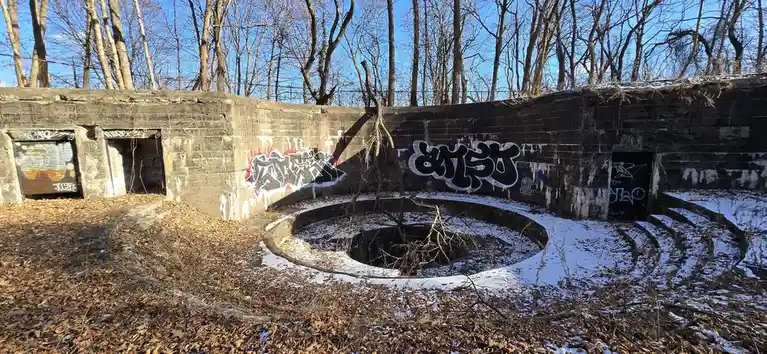 This image shows a dilapidated concrete structure, likely an old bunker or fortification, covered in graffiti and surrounded…