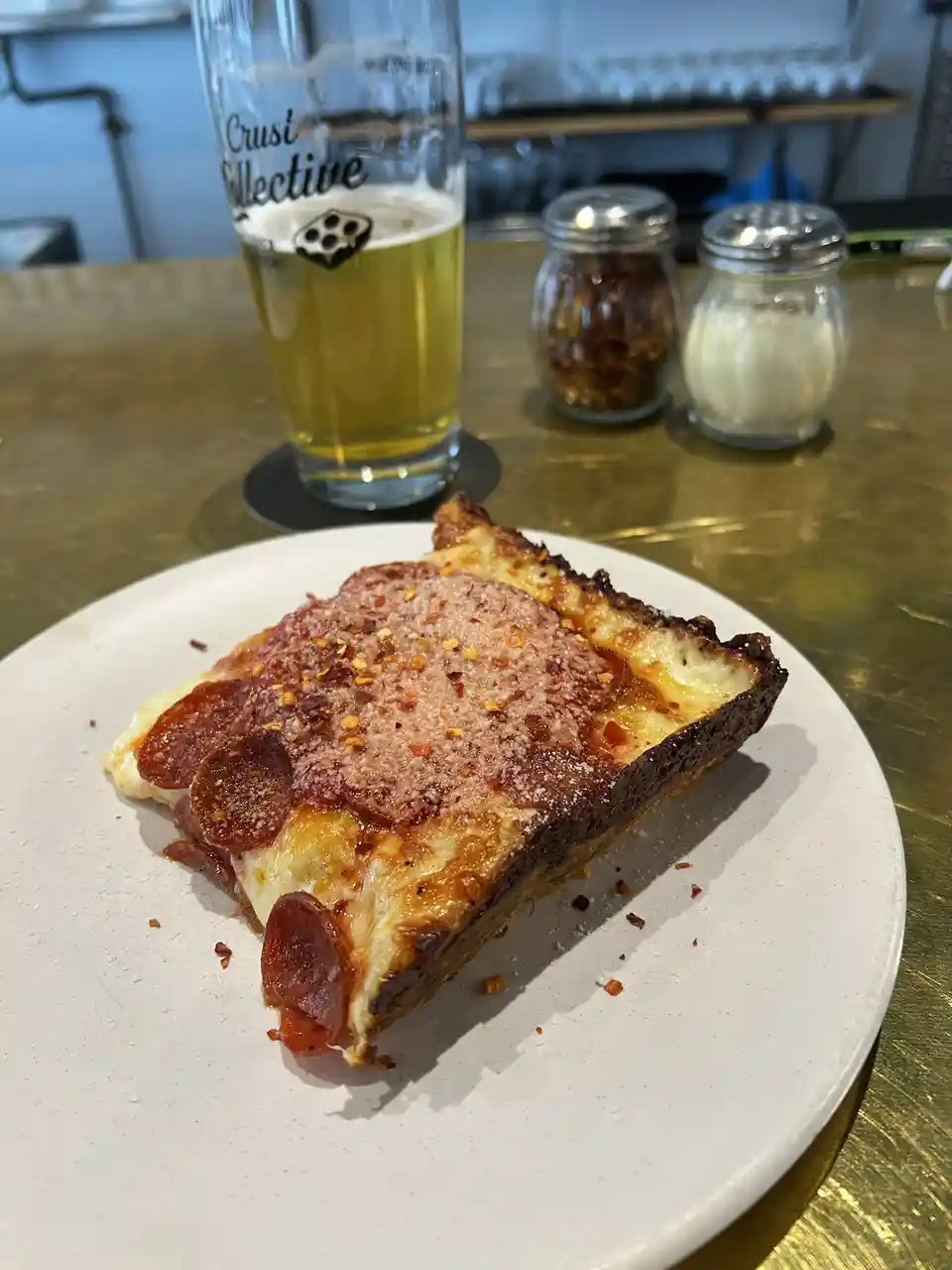 A close-up photo shows a thick, square slice of deep-dish pizza on a white plate, topped with pepperoni, melted cheese, and…