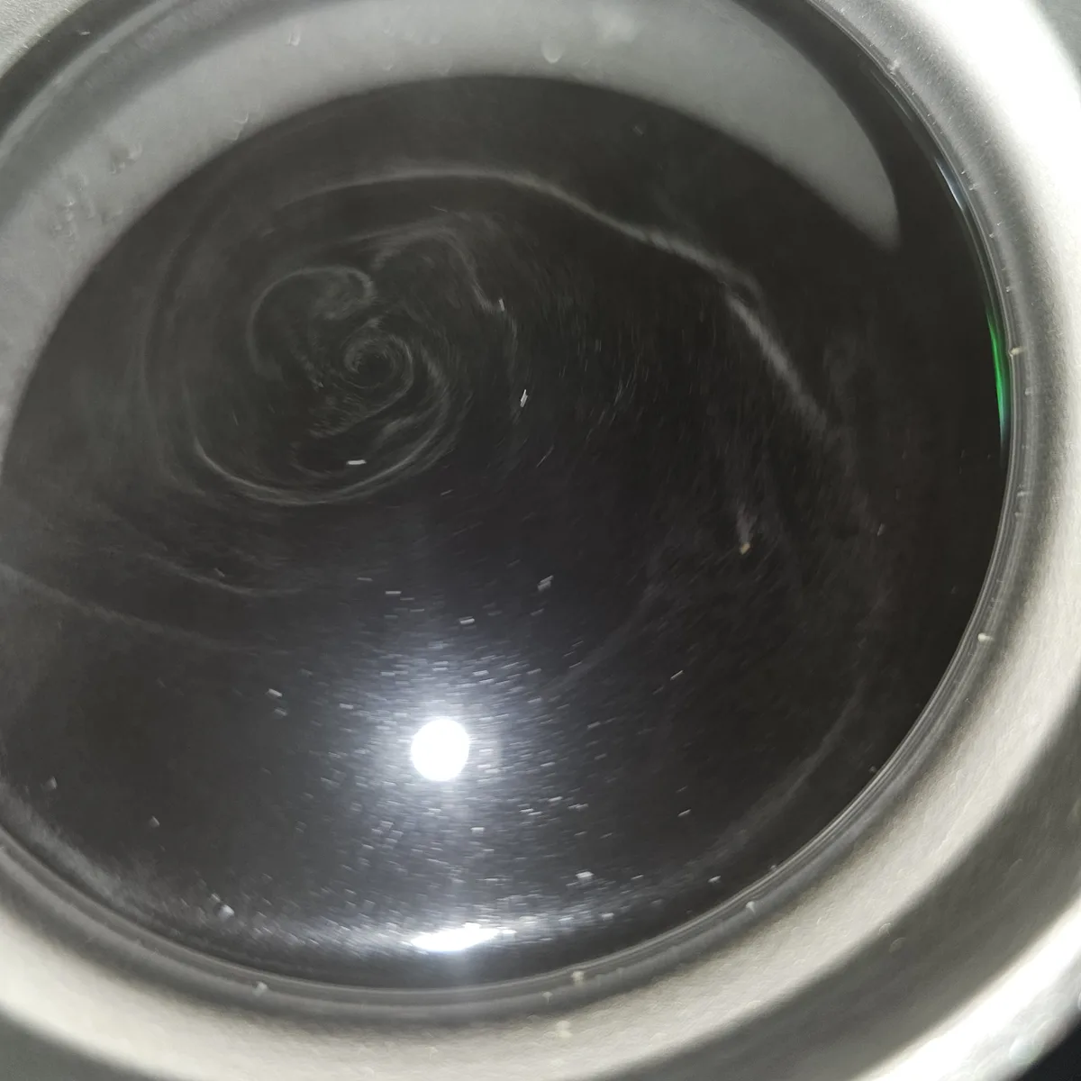 A top-down view inside a dark, swirling, circular container, possibly a washing machine drum, with a bright light reflection…
