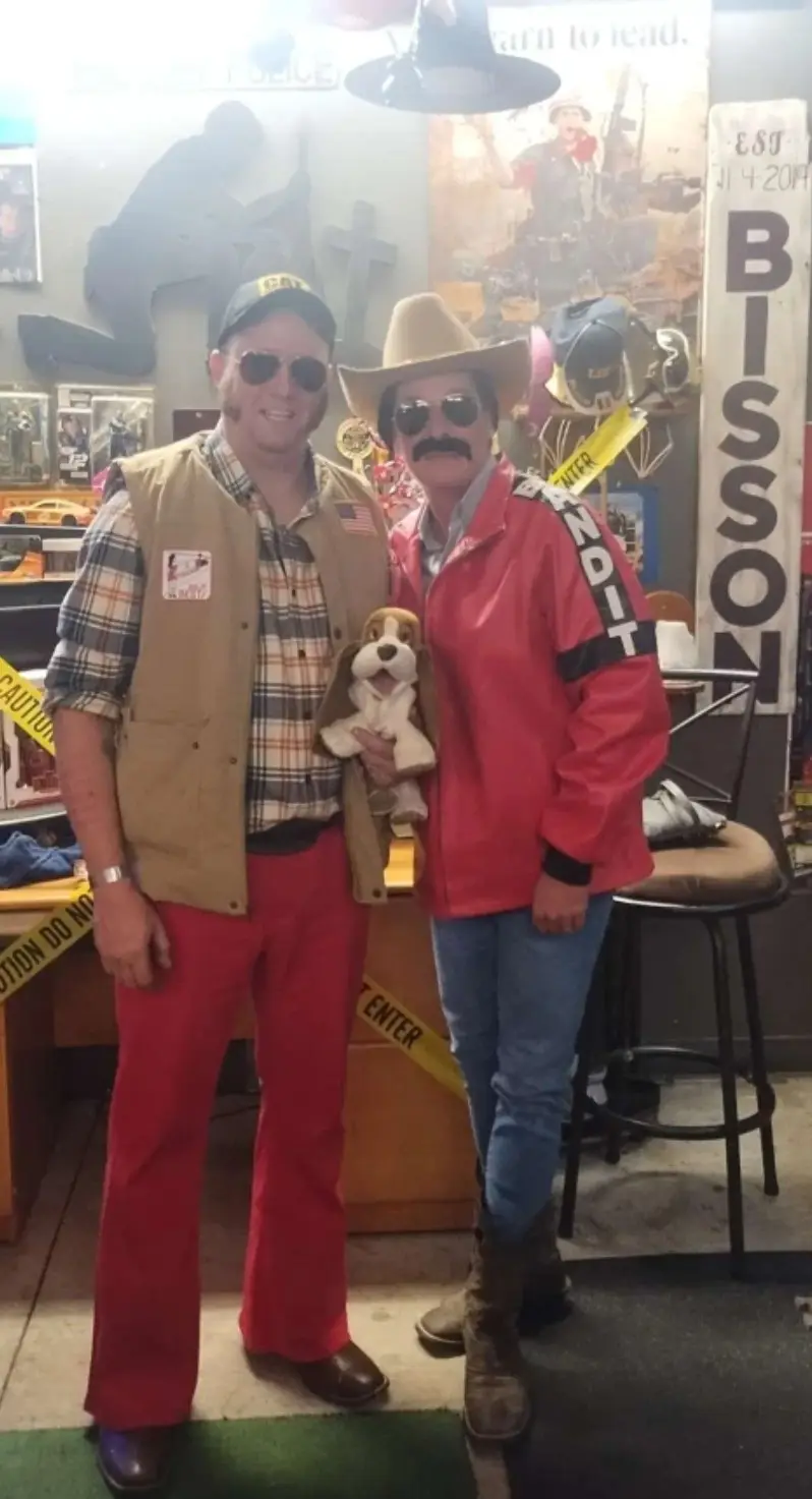 Two men dressed as characters from the movie 'The Dukes of Hazzard' pose for a photo in a room decorated with memorabilia…