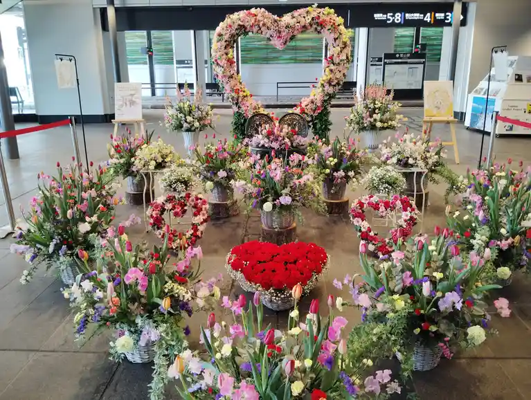 a train station concourse is decorated with numerous colorful floral arrangements, including large heart-shaped displays…