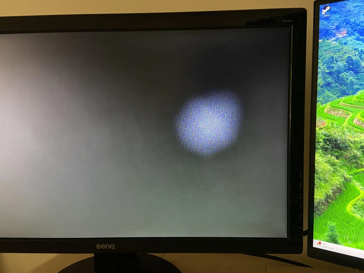 A BenQ monitor displays a single, blurry, pixelated blue circle on an otherwise blank gray screen, with a second monitor to…