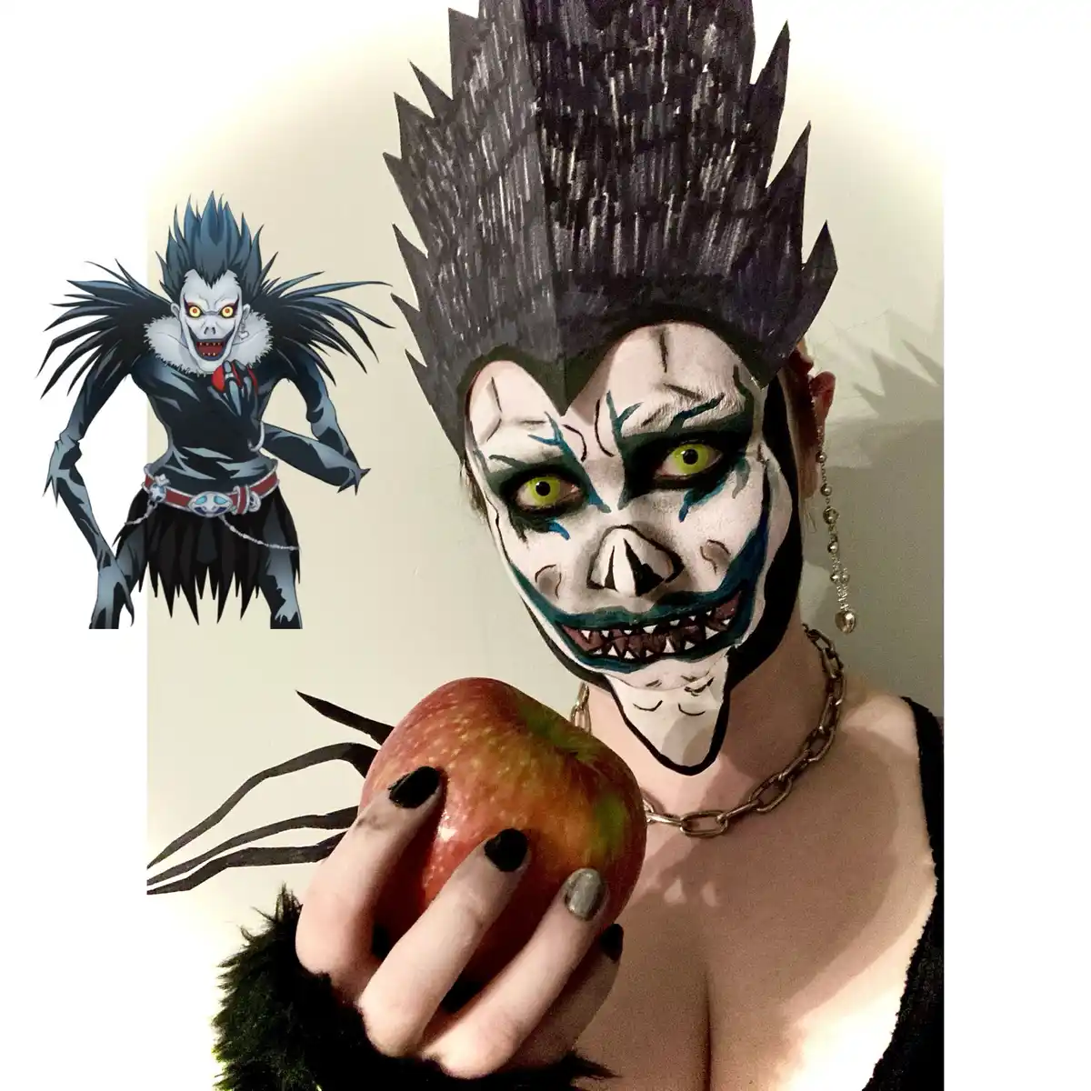 A person with elaborate white and black face paint resembling the anime character Ryuk from Death Note, holding an apple…