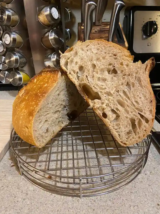 A freshly baked, artisanal loaf of bread is sliced open and displayed on a metal cooling rack in a kitchen. The interior…