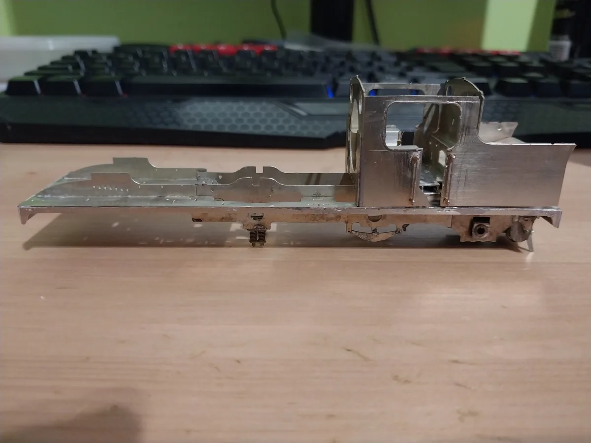 A partially assembled metal train model sits on a wooden desk, with a black keyboard featuring red and blue backlighting…
