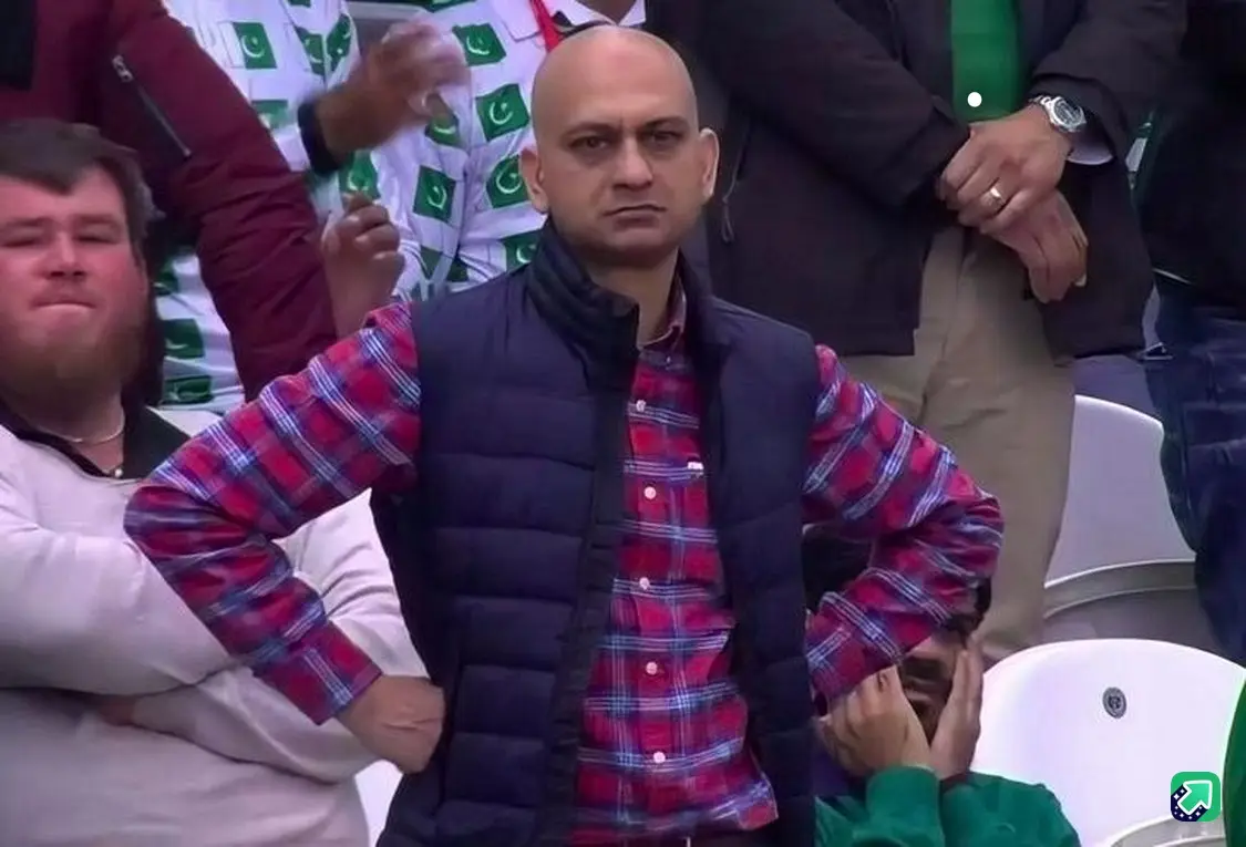 A bald man in a red plaid shirt and dark vest stands with hands on hips in a stadium, looking intensely displeased…