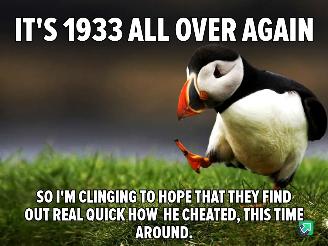 A photograph of a puffin standing on green grass with a blurred background, looking down and to the side. The image has…