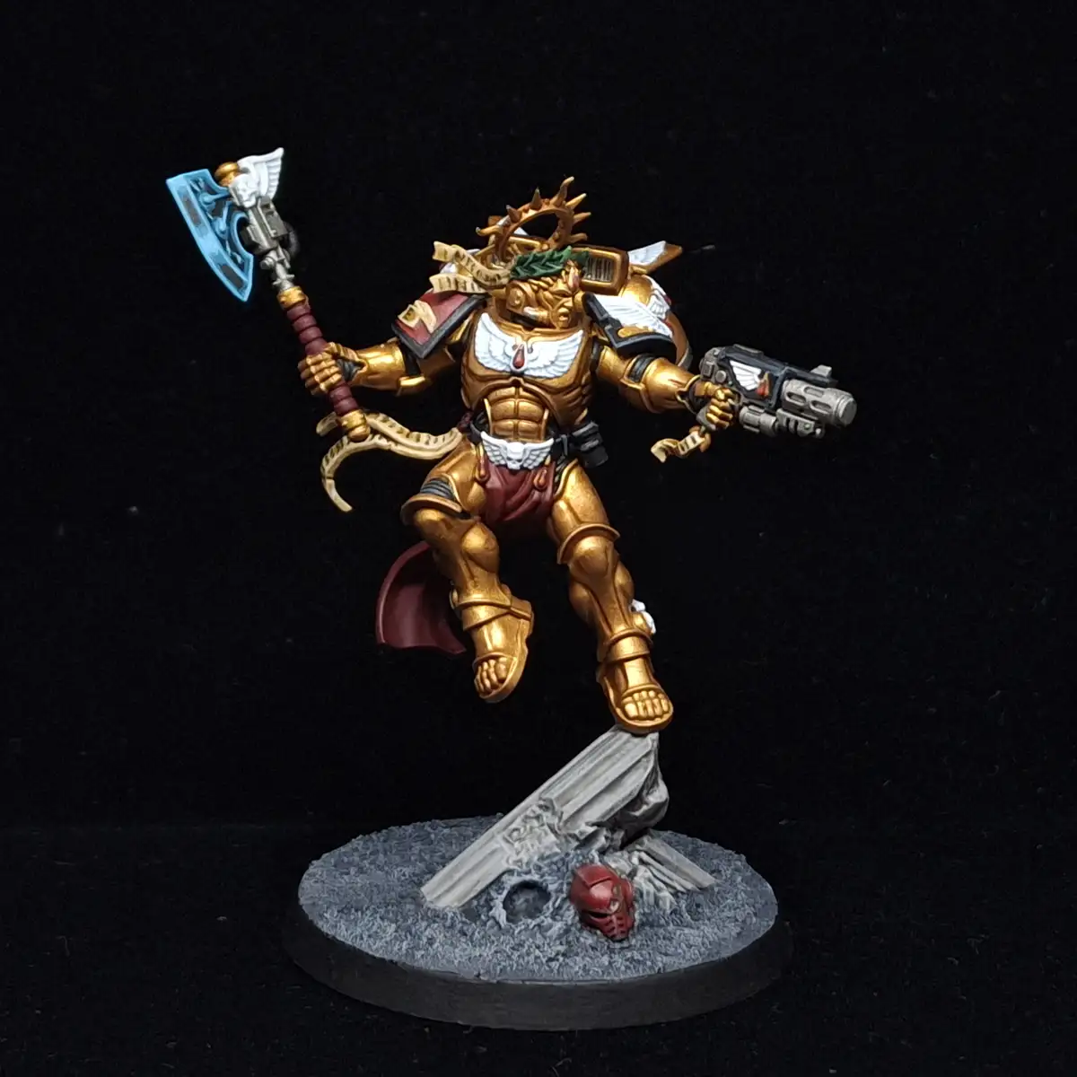 A heavily painted miniature of a golden-armored warrior, likely from Warhammer 40,000, stands triumphantly on a rocky base…