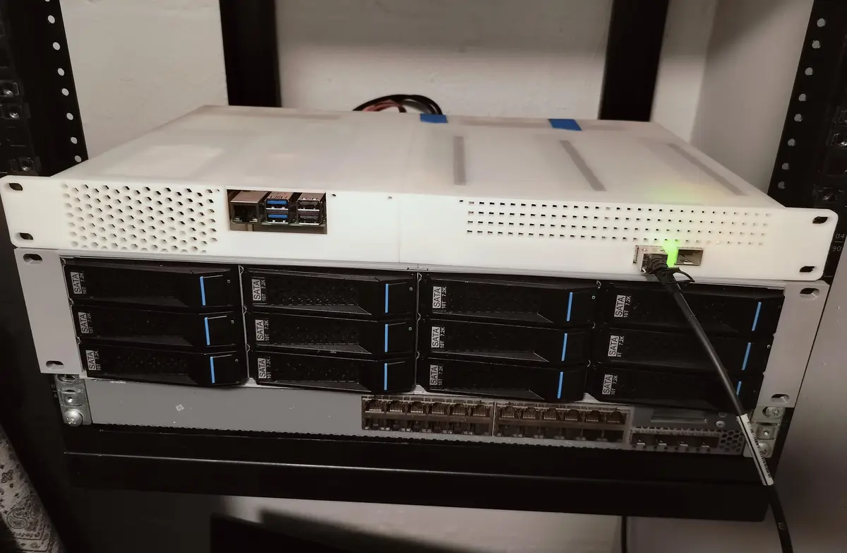 A white 3d-printed server rack sits atop a standard black server rack, both mounted in a server cabinet. The top unit has…