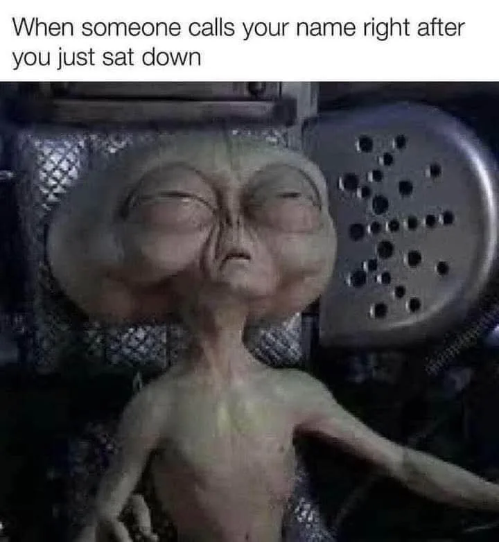 A pale, thin alien with large, bulging eyes and a long neck is shown reclining in a metallic, industrial-looking chair with…
