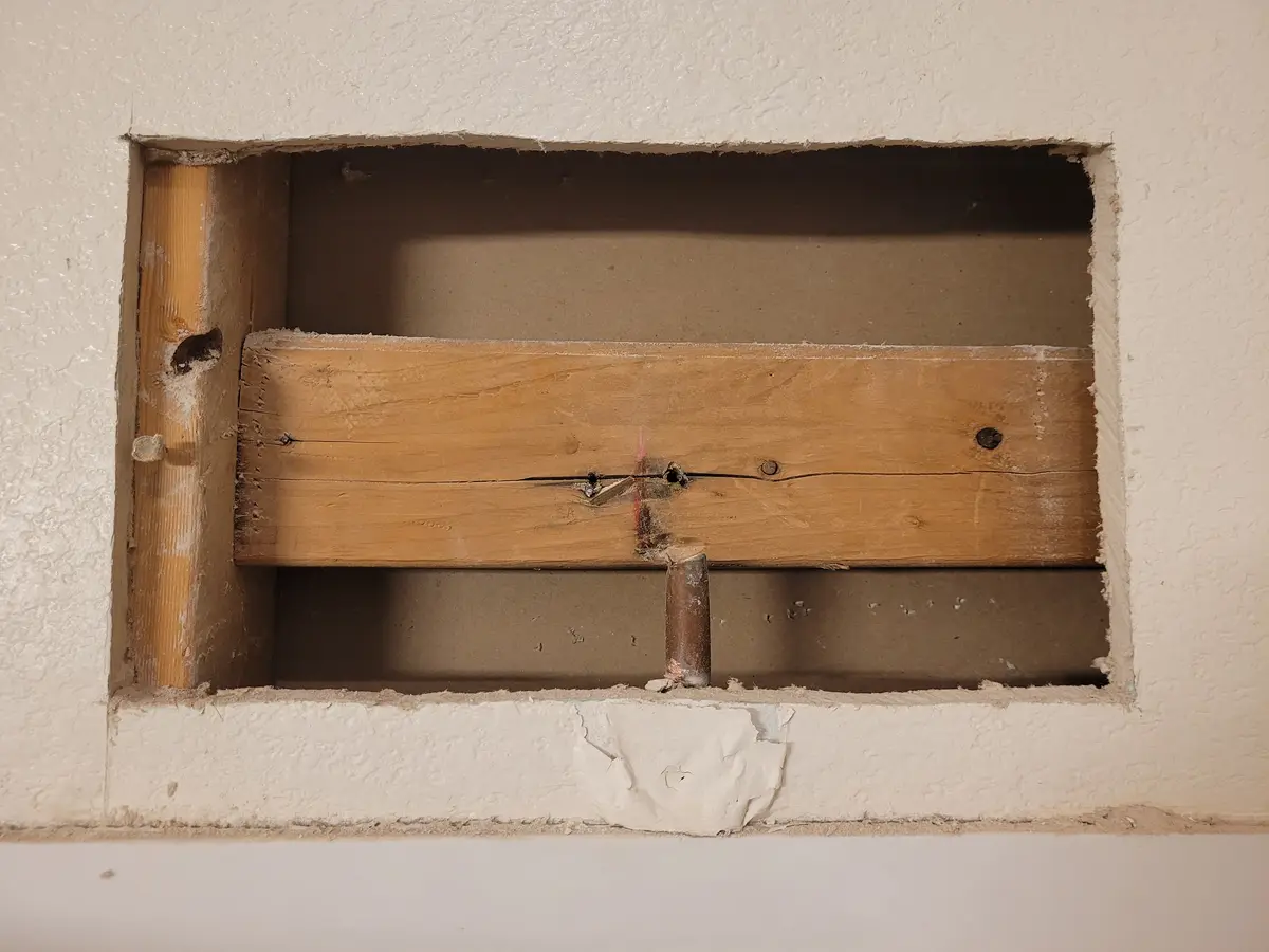 A rectangular hole in a white textured wall reveals exposed wooden framing and a rusty pipe. The overlaid text reads 'i just…