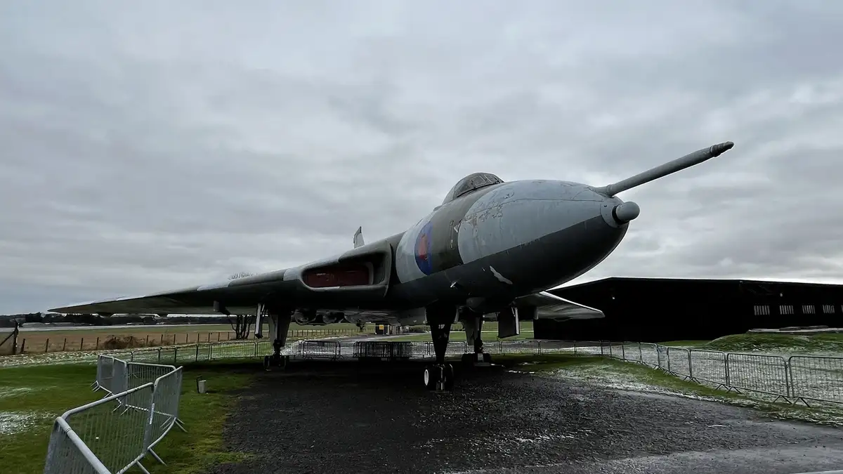 A vintage military jet aircraft, likely a British Avro Vulcan, is displayed outdoors on a cloudy, overcast day with patches…