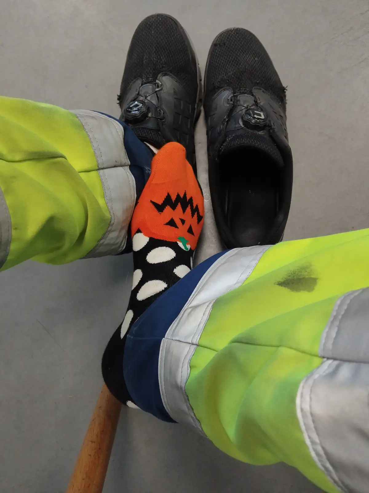 A person wearing bright yellow high-visibility work pants and black cycling shoes with BOA closures is sitting down, with…
