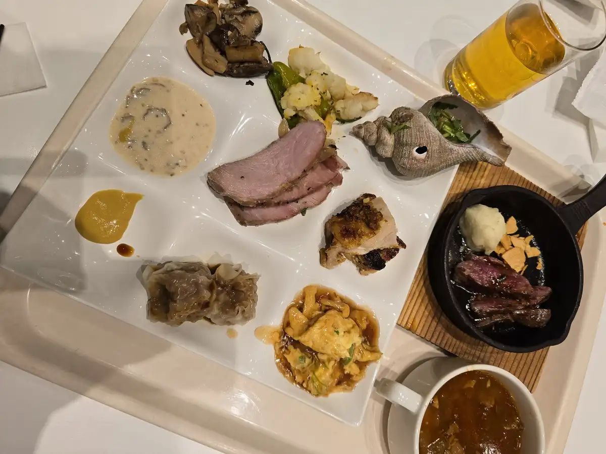 A white tray holds an elaborate, multi-course meal with various dishes including sliced meat, mushrooms, cauliflower…