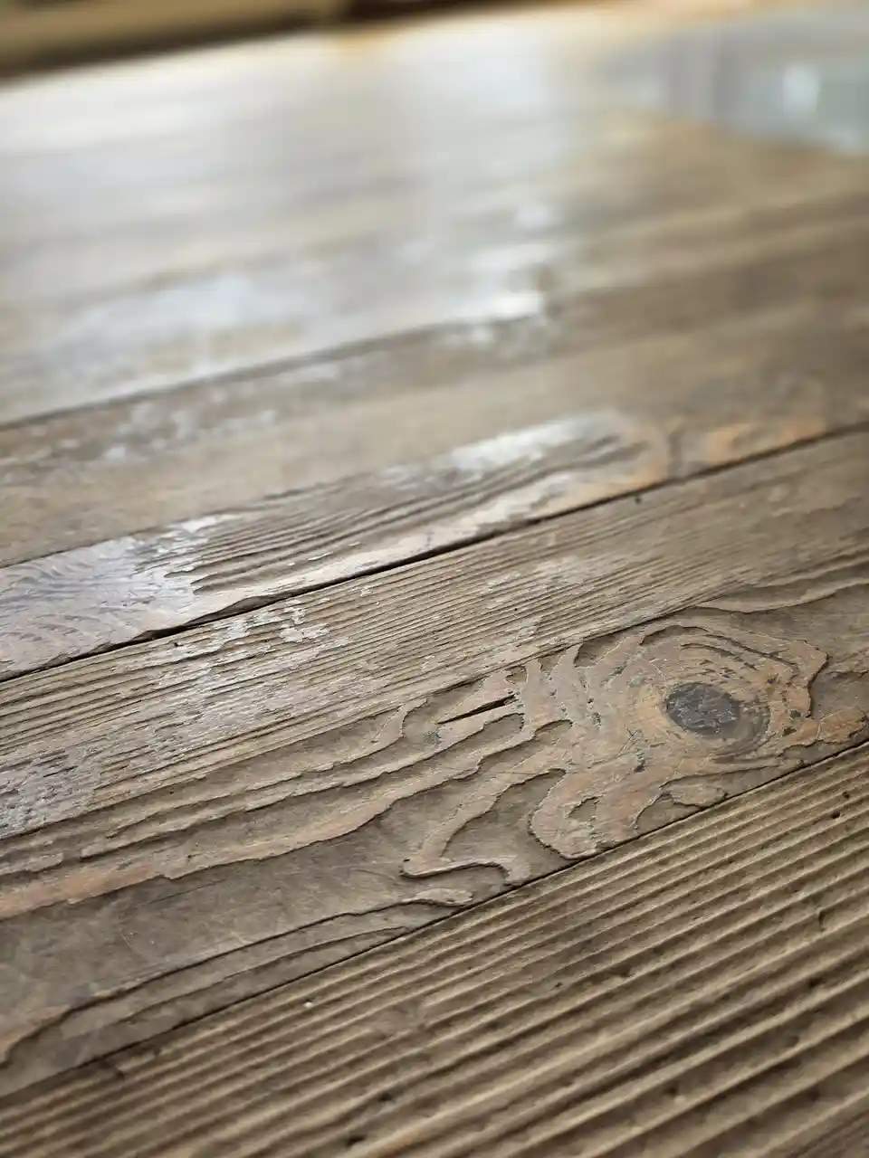 A close-up photograph of a weathered wooden surface with peeling paint and visible grain, where the texture of the wood…
