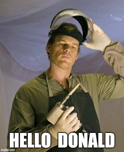 A man in a welding apron and gloves holds a welding torch while lifting a welding helmet off his head, revealing his face…