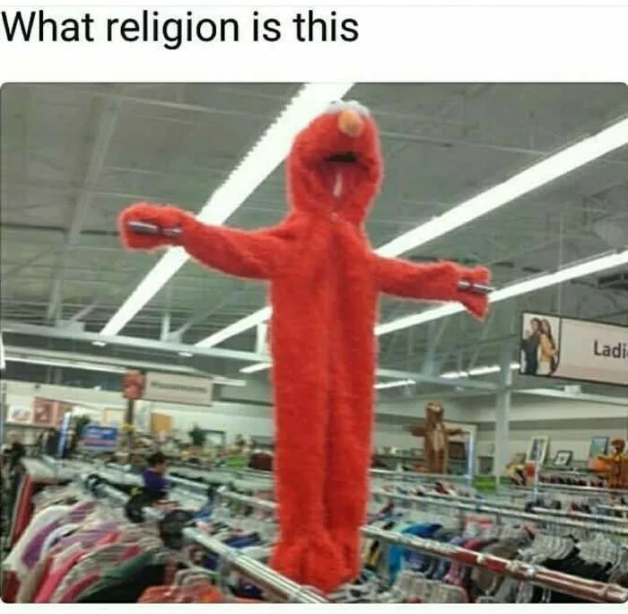 A person in a full-body red Elmo costume stands in a clothing store aisle with arms outstretched, mimicking the pose of a…