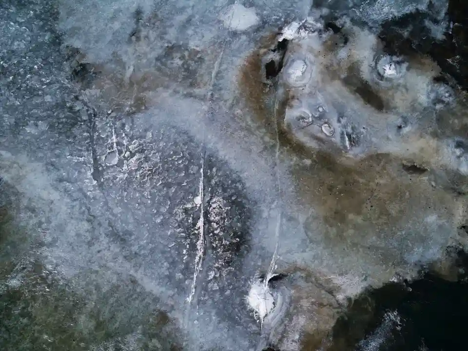 An aerial view of a frozen body of water with cracked ice, dark patches, and white snow, overlaid with the text 'i'm not a…