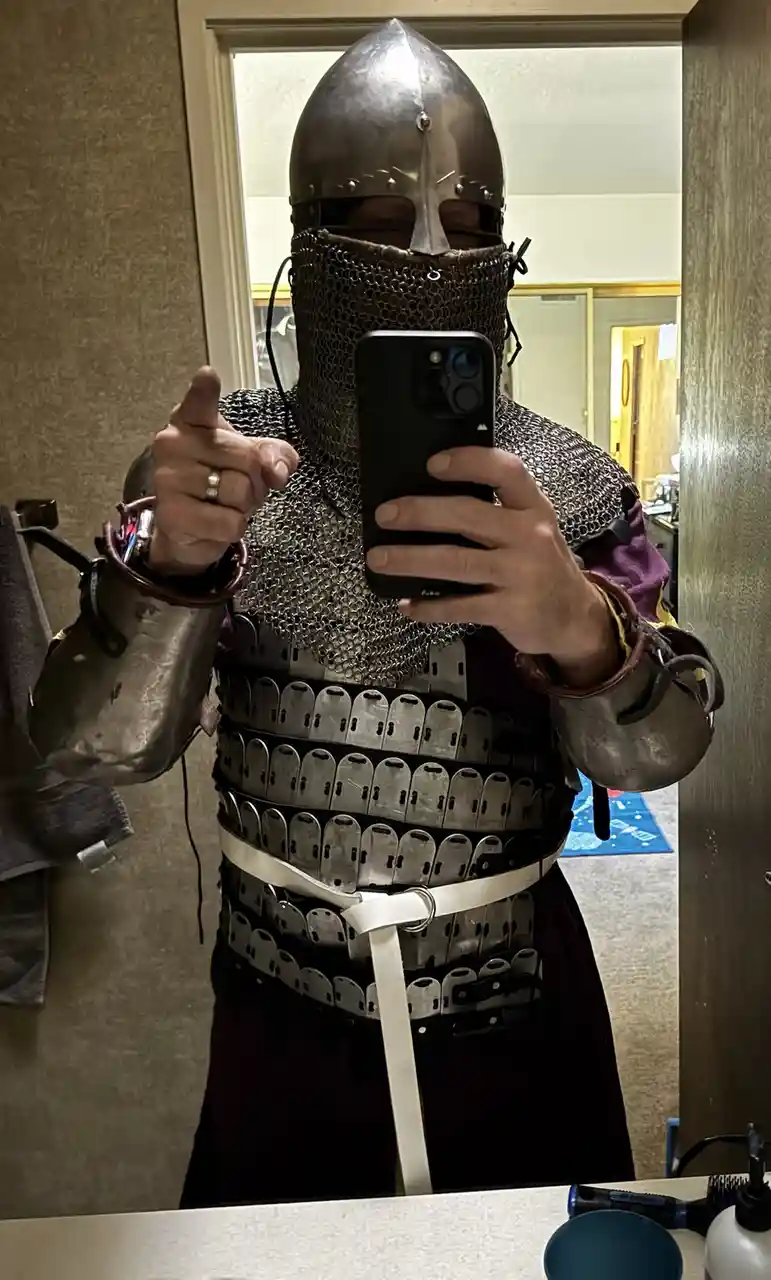 A person wearing full medieval-style armor including a helmet with a visor, chainmail coif, and a segmented plate cuirass…