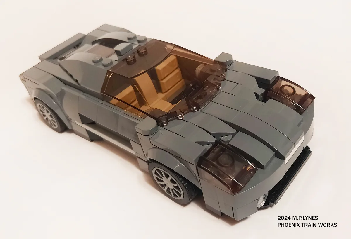 A grey Lego model of a futuristic sports car with tan interior and transparent windows, photographed on a white background…