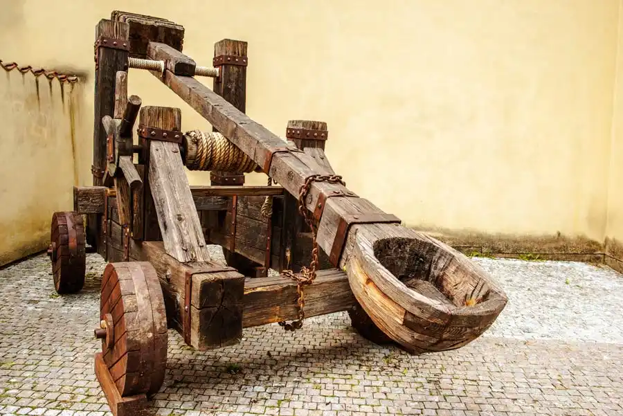 A large, wooden medieval-style catapult sits on a cobblestone surface against a plain wall. The overlaid text reads 'i'm not…