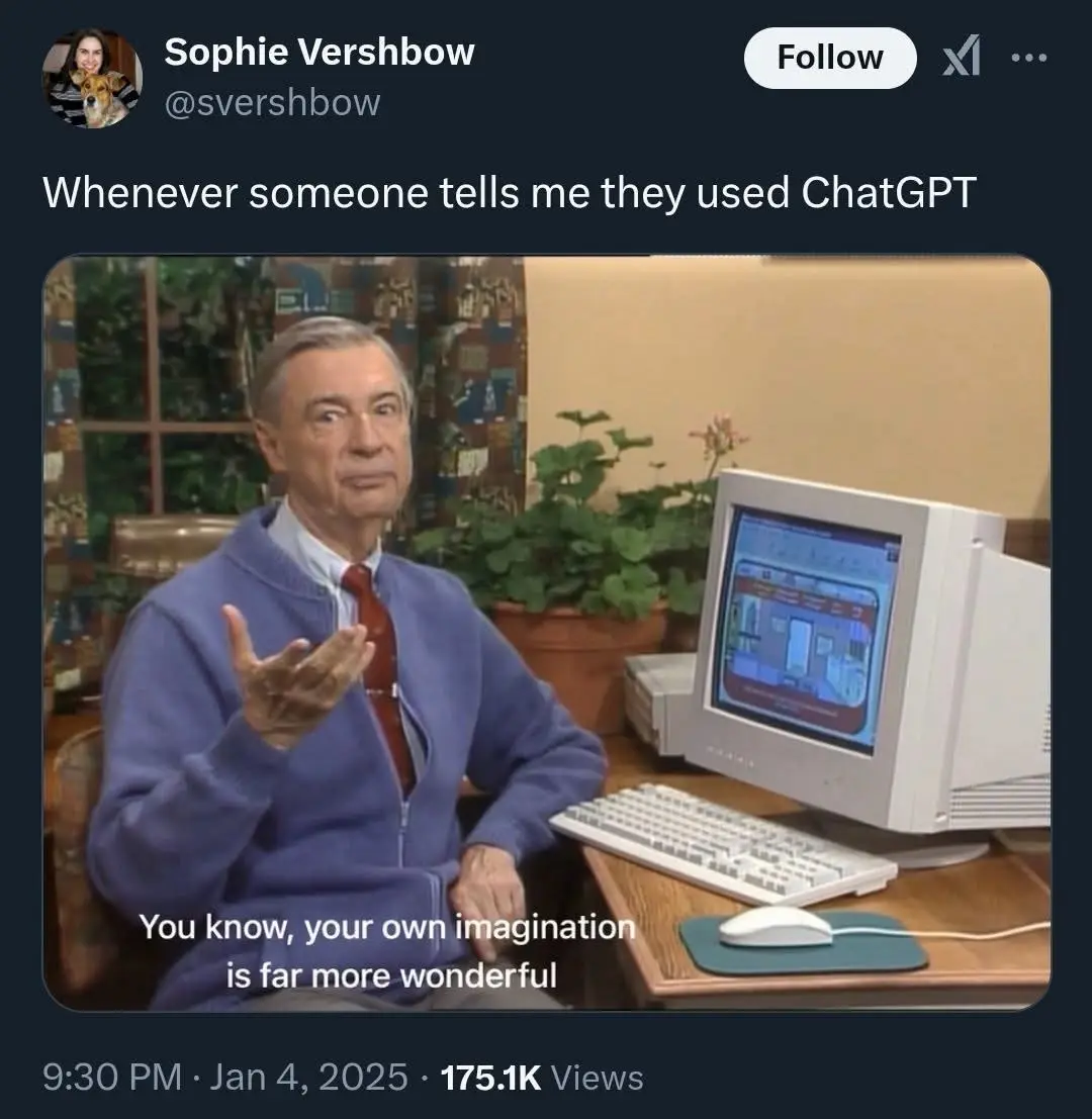 A man in a blue zip-up sweater and red tie sits at a desk with a white CRT computer, keyboard, and mouse. He gestures with…