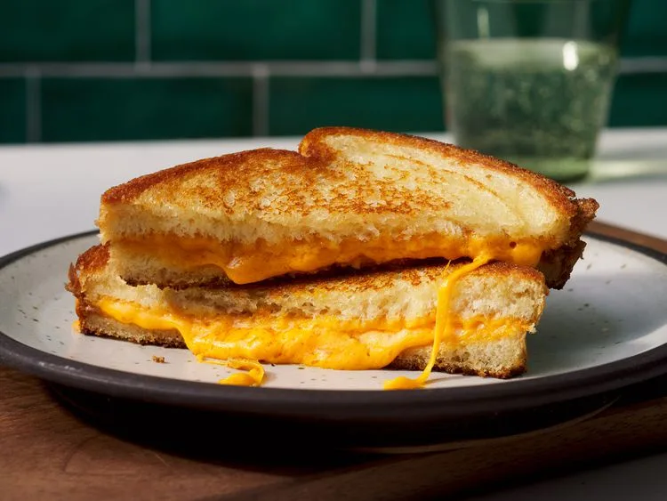 a perfectly grilled cheese sandwich, cut in half and stacked, with molten orange cheese oozing out from between the…