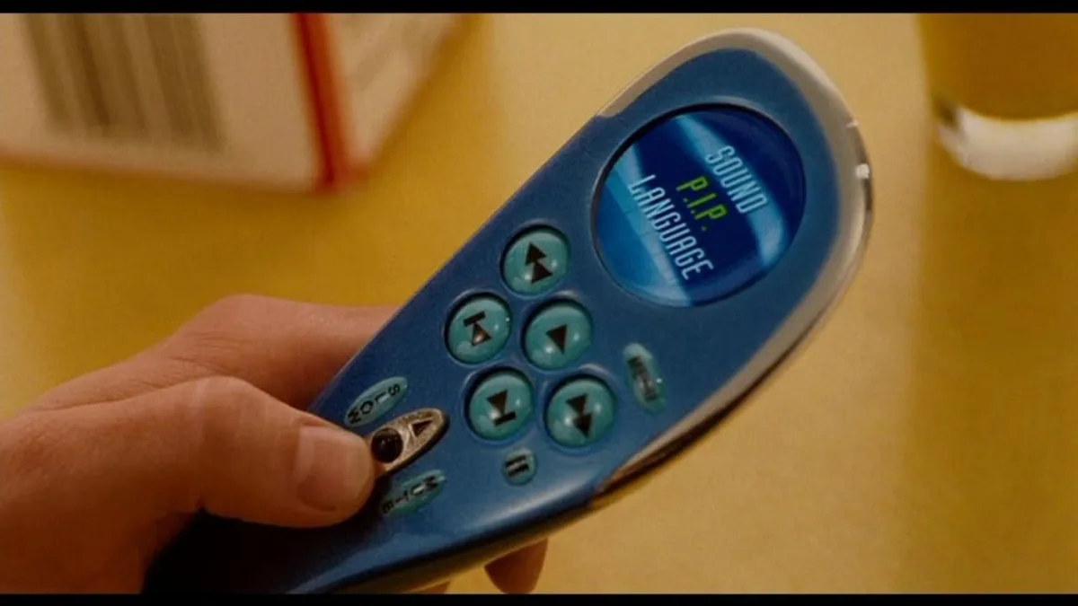 A close-up shot of a hand holding a blue, oval-shaped remote control with a small screen displaying the words 'SOUND'…