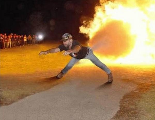 A man in a baseball cap and t-shirt is mid-motion, arms extended as if throwing something, with a large fiery explosion…
