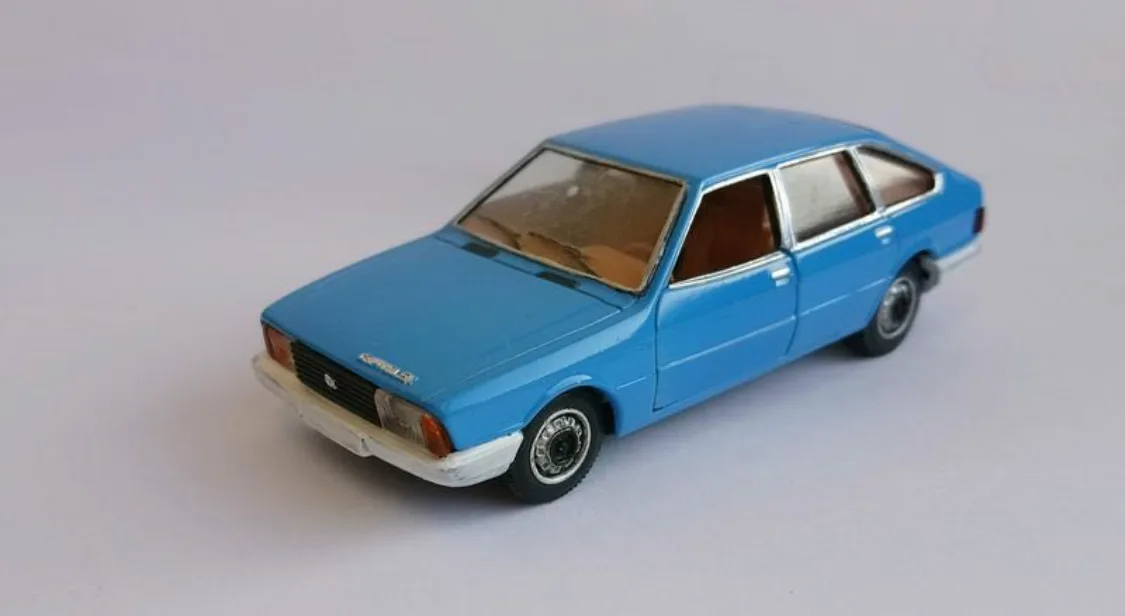 A blue toy car model, likely a Peugeot 504, is photographed against a plain white background. The car has a slightly worn…