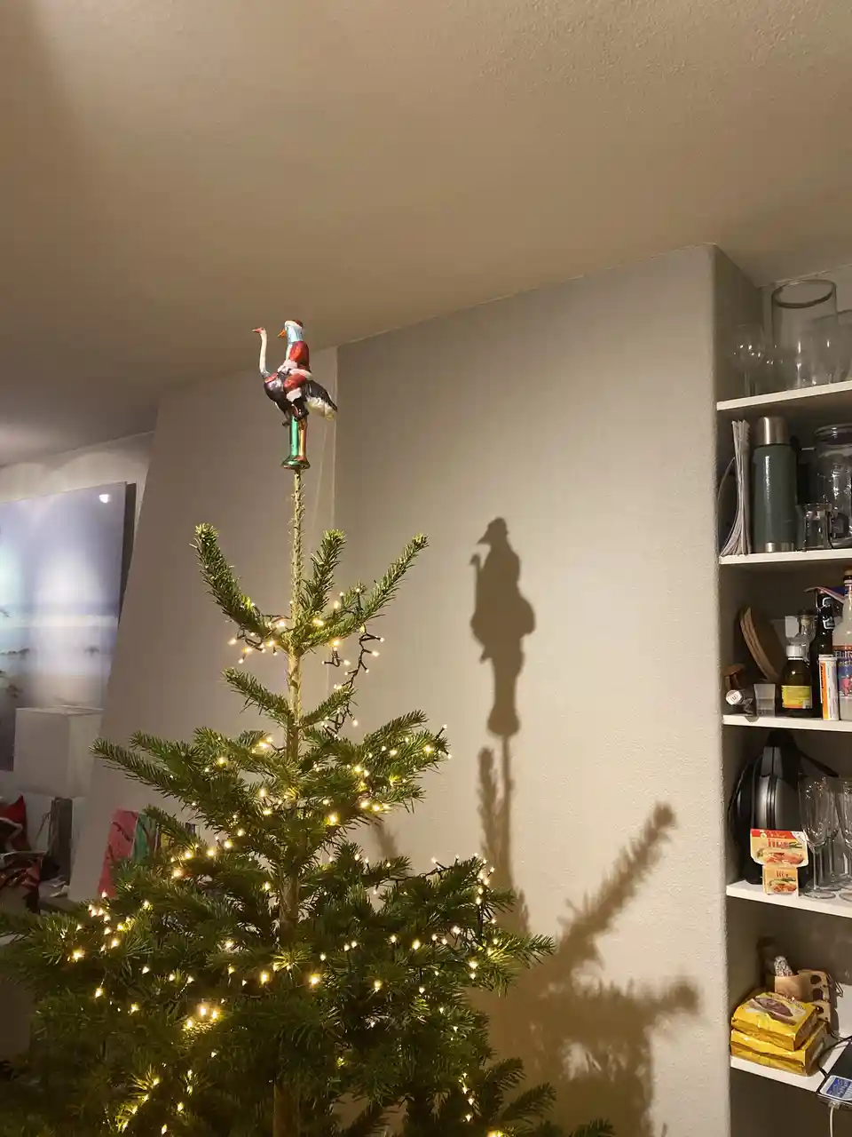 A decorated christmas tree with warm string lights has a whimsical topper: a small figurine of santa claus riding an…