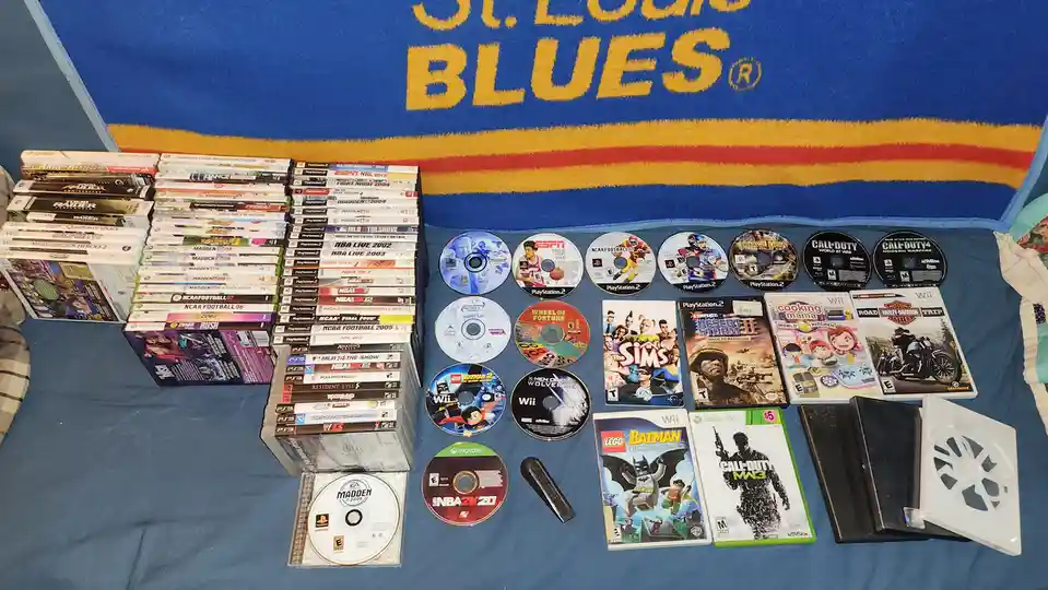 A large collection of video game cases and discs from various consoles like PlayStation 2, Xbox 360, Wii, and PS3 are laid…