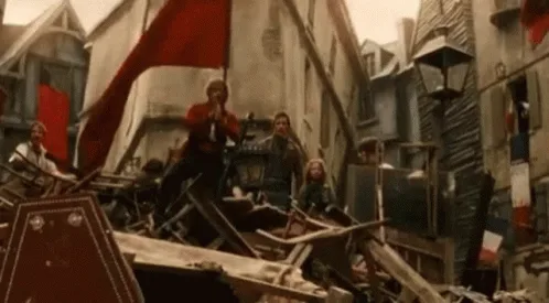 A sequence of frames from a historical film shows a man in a red jacket waving a red flag atop a barricade made of debris in…
