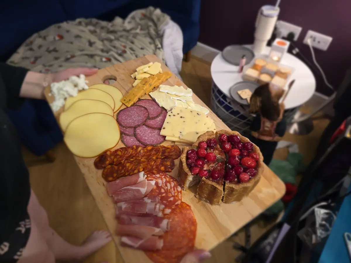 A person holds a large wooden charcuterie board filled with various cheeses, cured meats like salami and prosciutto…