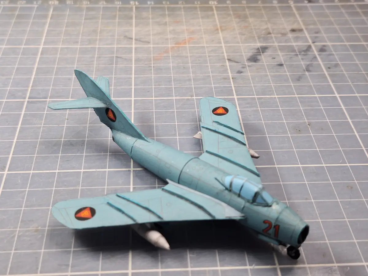 A light blue model airplane with red and black roundels on its wings and tail, and the number 21 on its nose, rests on a…