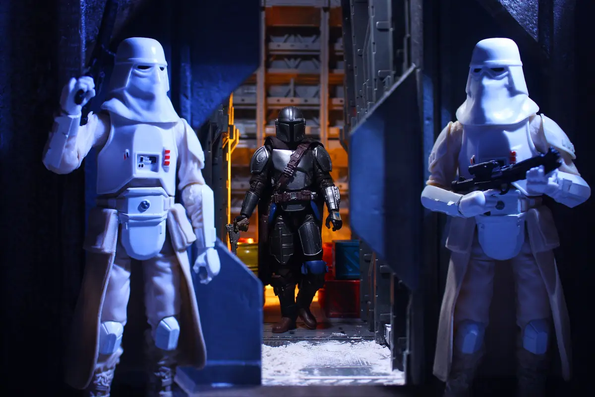 Two white-armored stormtrooper action figures stand guard on either side of a doorway, facing inward, while a central figure…