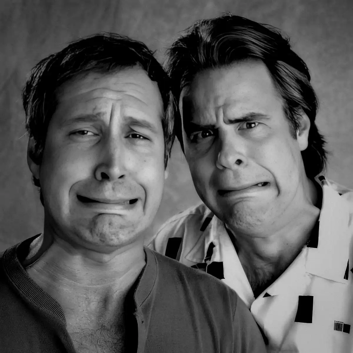 A black-and-white photo shows two men with exaggerated, sorrowful facial expressions. The man in the foreground has tears…
