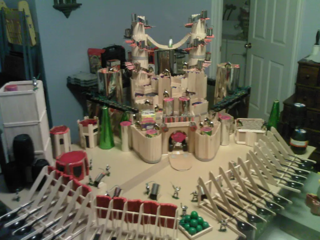 A large, elaborate castle model constructed from kitchen utensils like spoons, forks, and bottle caps, with tiny figurines…