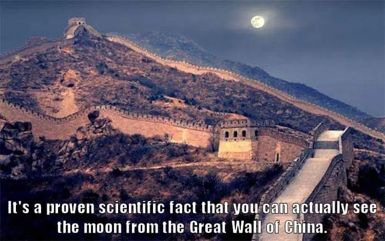 A nighttime photograph shows the Great Wall of China snaking across rugged, treeless hills under a bright, full moon. The…