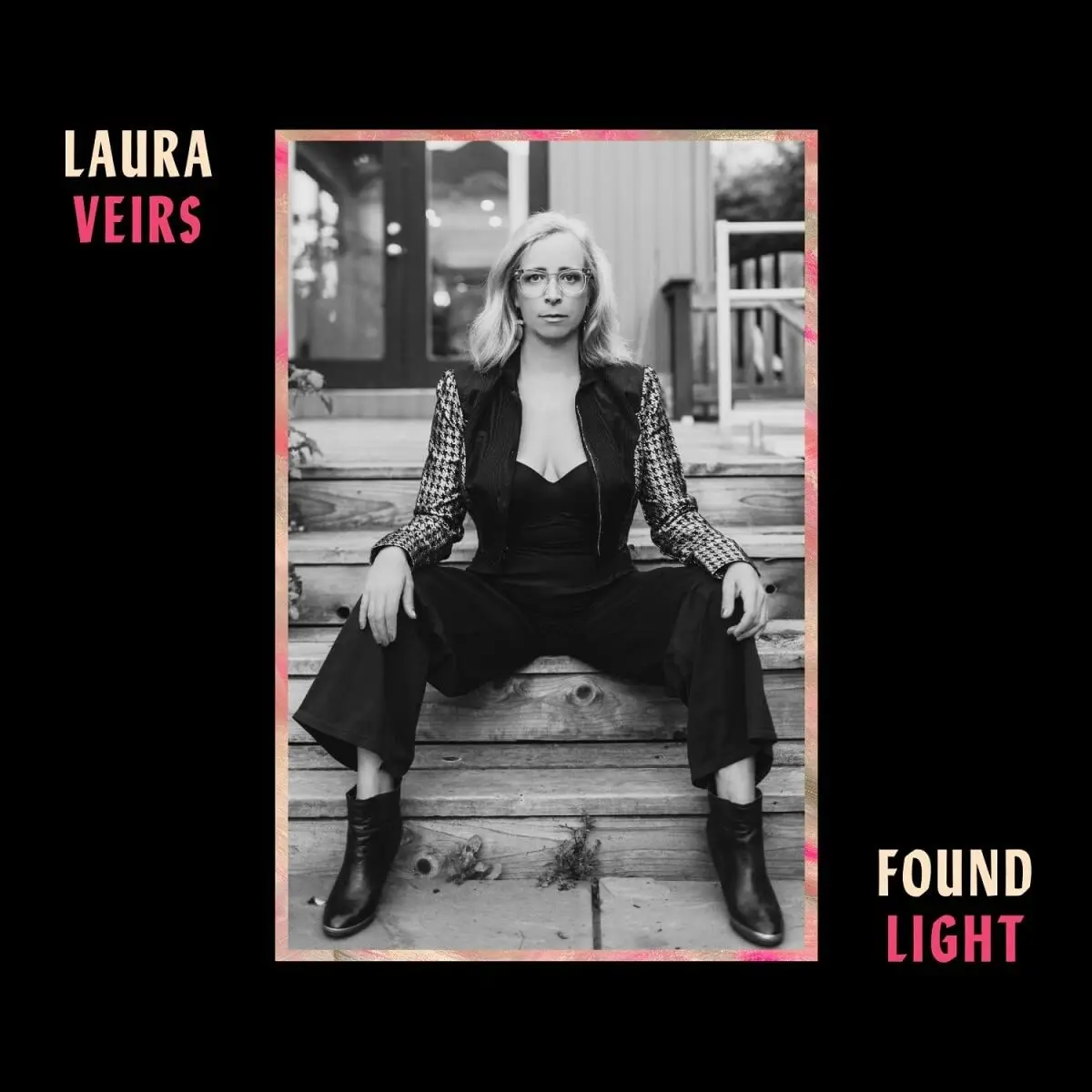 A black-and-white photo of musician Laura Veirs sitting on wooden steps, wearing glasses, a black outfit with houndstooth…