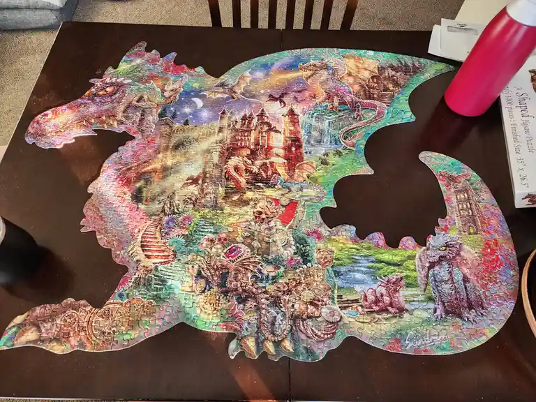 A completed 1000-piece jigsaw puzzle shaped like a dragon, featuring fantasy scenes with castles, dragons, and treasure…