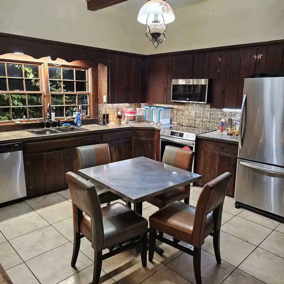 A kitchen with dark wood cabinets, stainless steel appliances including a refrigerator and microwave, and a dining table…
