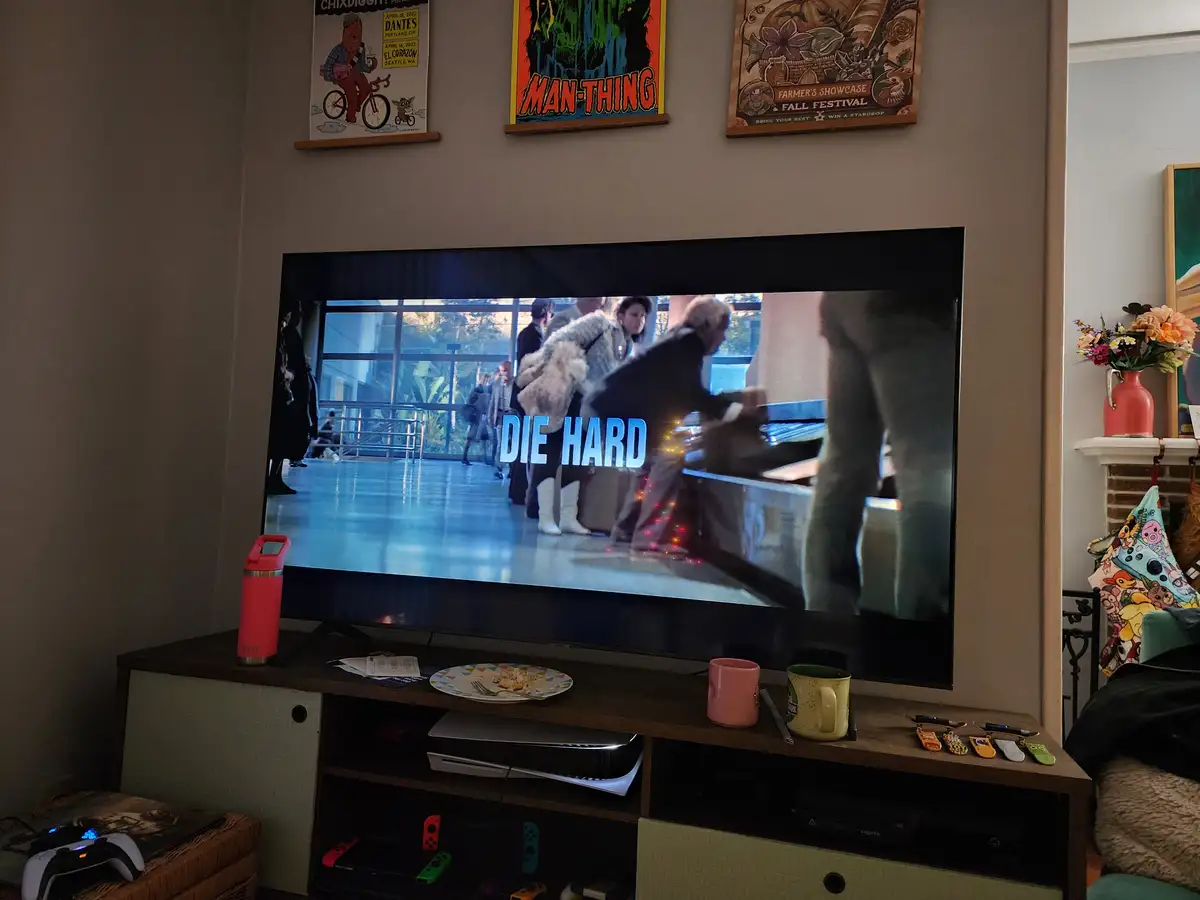 A television in a living room displays a scene from the movie 'Die Hard' with the title overlaid in large blue letters. The…