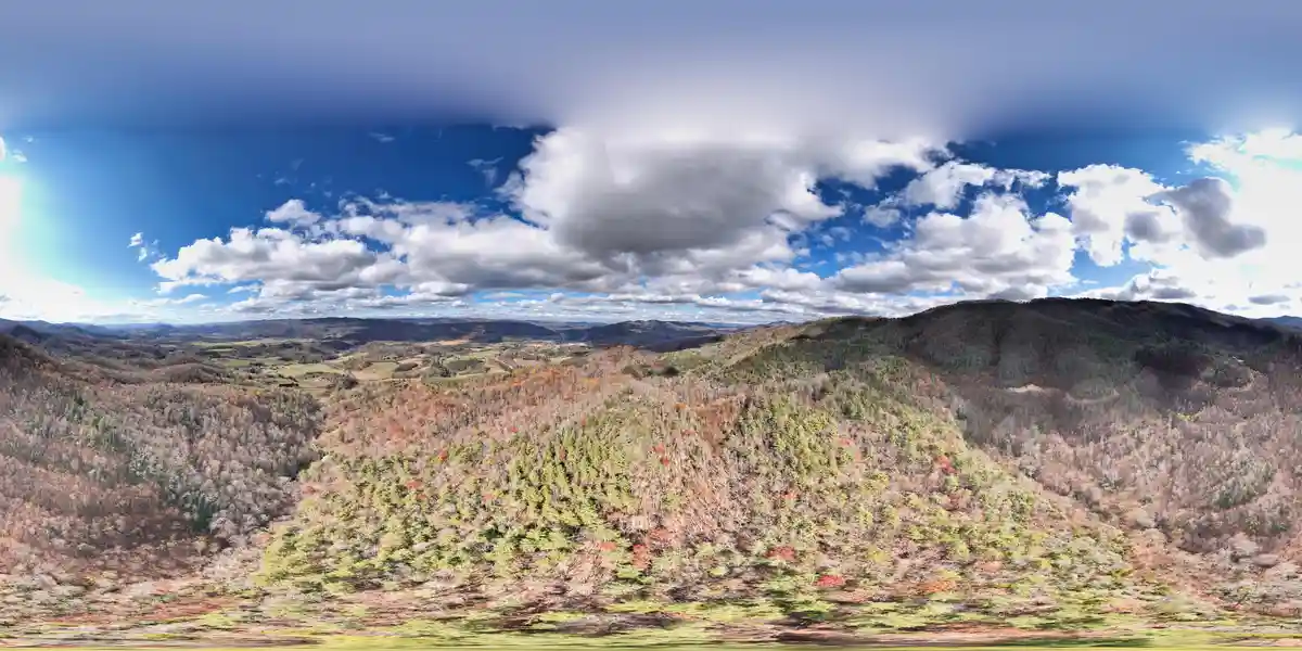 A panoramic 360-degree view of rolling hills covered in autumn foliage under a partly cloudy blue sky. The image is overlaid…