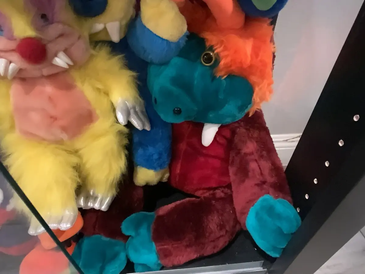 A close-up photo shows several colorful, fuzzy plush monsters with exaggerated features like sharp teeth and claws, huddled…